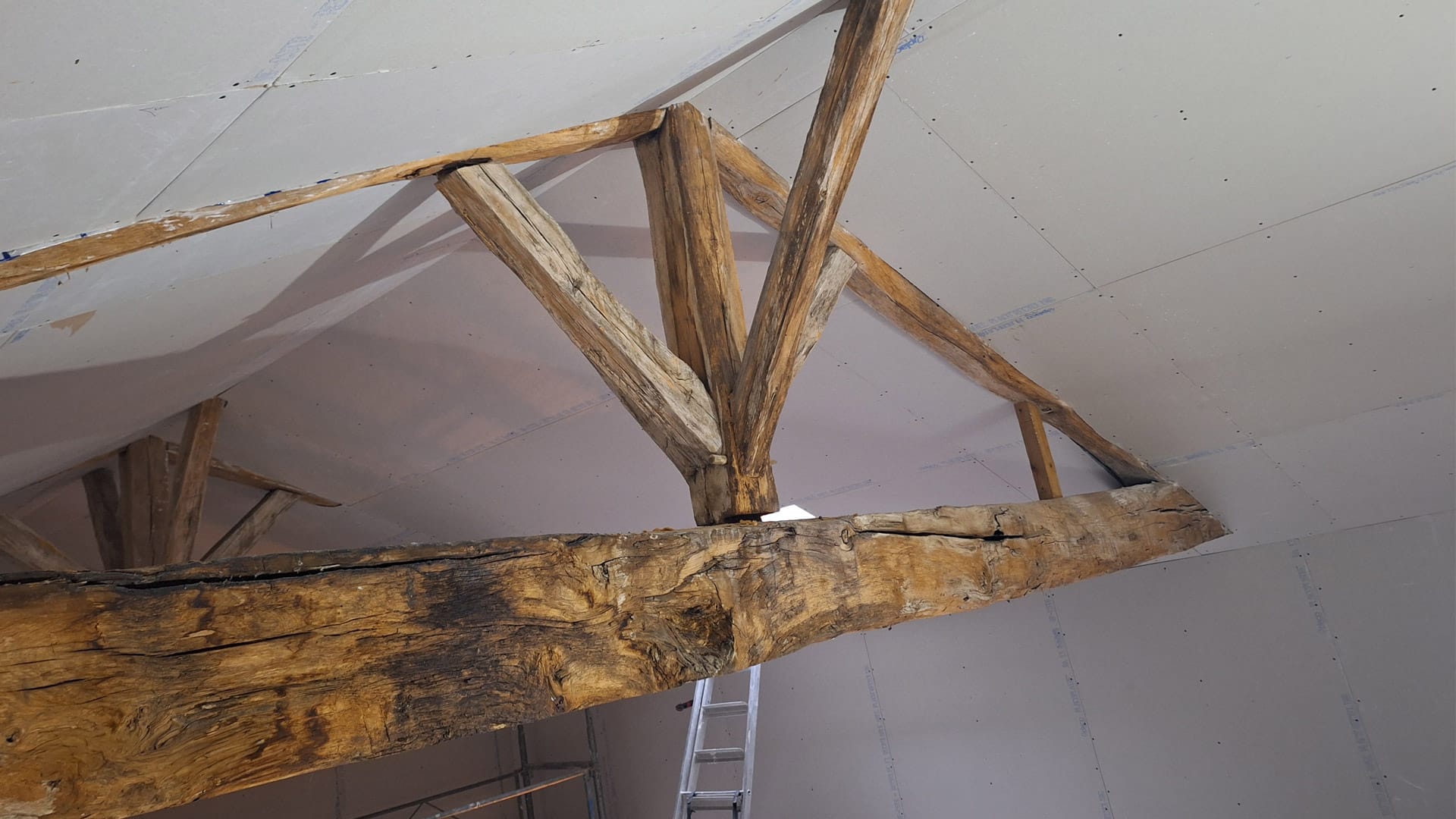 Charpente en bois apparent avec poutres anciennes et assemblage traditionnel, en cours de rénovation sous un plafond en plaques de plâtre