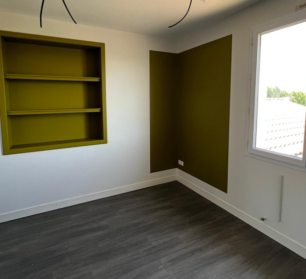 Pièce vide avec un mur vert foncé, une étagère encastrée jaune, sol stratifié gris foncé et une fenêtre laissant entrer la lumière naturelle.